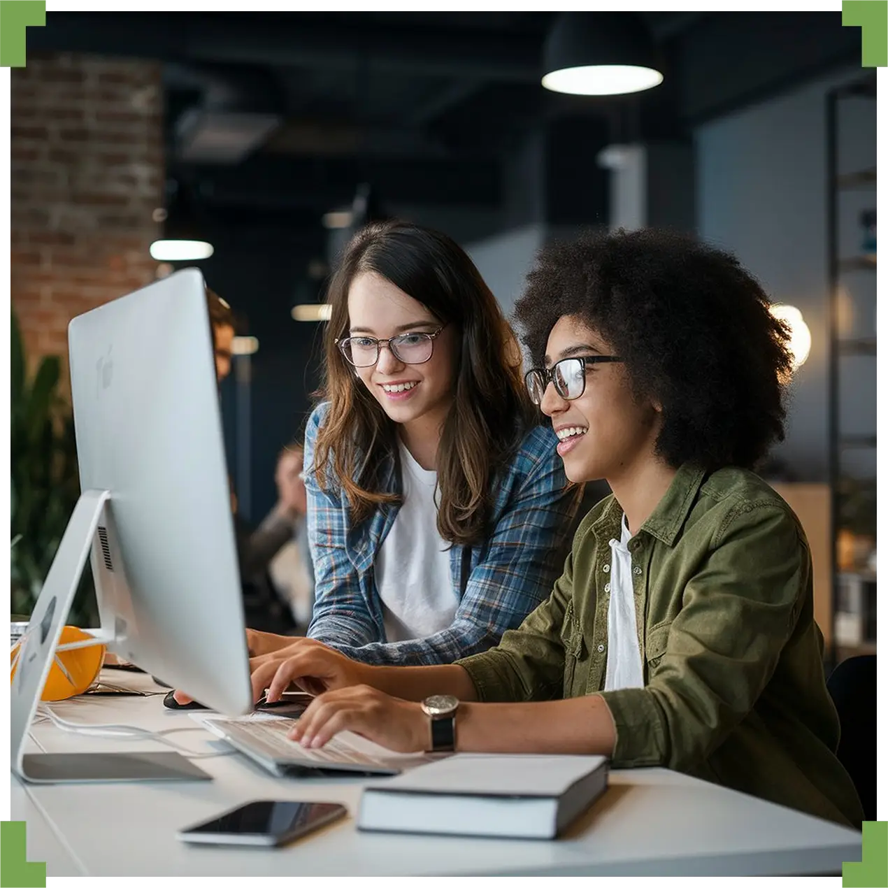 Two women working together at a desk environment in an office space.